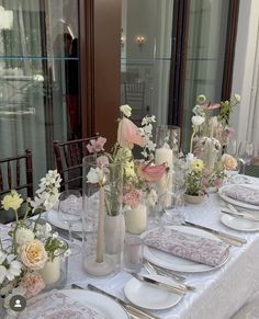 the table is set with white and pink flowers in glass vases, plates and silverware