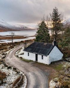 an old white house sitting on the side of a road next to a body of water