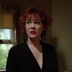 a woman with red hair in a black shirt and earrings looking off into the distance