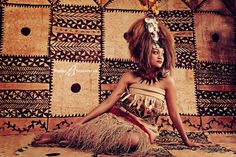 a woman sitting on the ground in front of a wall with decorative designs and feathers