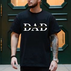 a man wearing a black t - shirt with the word dad printed on it, standing in front of a green door