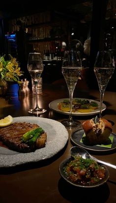 a table topped with plates of food next to wine glasses and utensils on top of a wooden table