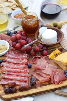 an assortment of cheeses, meats and fruit on a wooden platter with crackers