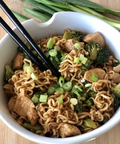 a bowl filled with noodles, broccoli and chicken on top of a wooden table