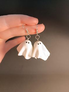 a person holding two white ghost earrings in their hand