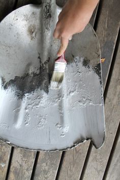 a person holding a paintbrush on top of a piece of metal with wood planks in the background