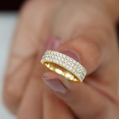 a woman's hand holding a yellow gold ring with white diamonds on the band