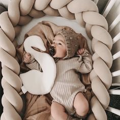 a baby is laying down in a basket made out of rope and pillows with a knitted hat on it's head