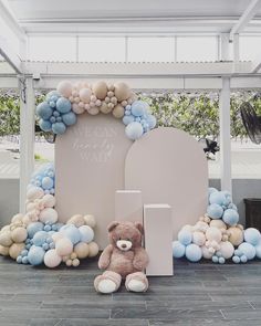 a teddy bear sitting in front of a large arch with balloons on the sides and a sign that says it's my first birthday