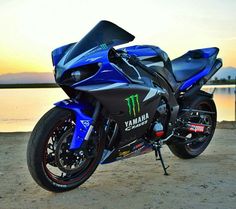 a blue motorcycle parked on top of a sandy beach next to the ocean at sunset