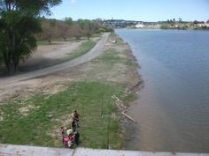 two people are standing on the edge of a river looking down at some water and grass