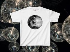 Classic 90s Disco ball baby tee. This tee is not cropped. Please refer to the size guide for your correct sizing. As these tees are custom made we are unable to offer returns due to wrong sizing. Please ensure you are measuring for sizing, if you are unsure I recommend comparing it to a tee you already own.  - 100% cotton (except for dark heather which is 50% cotton & 50% polyester) - Medium fabric (5.3 oz/yd² (180 g/m - Semi-fitted FAQ - How long will it take to receive my order? Production time: * 2-3 business days Delivery times: * USA = standard shipping: 2-5 business days = economy shipping: 4-8 business days  * United Kingdom: 5-7 days  * Europe: 5-10 days * Australia: 5-10 days * Canada: 5-10 days * Rest of the world: 7-10 days Disco Style White Top With Graphic Print, White Disco Style Tops With Graphic Print, White Disco Style Top With Graphic Print, 90s Disco, Pinterest Style, Mirror Ball, Fitted Tee, Baby T Shirts, Disco Ball