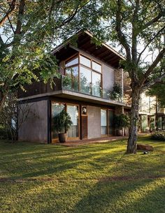 A imagem mostra um sobrado e um quintal. O sobrado é de arquitetura moderna, com linhas retas e fachada com acabamento em cimento/concreto, esquadrias em madeira e detalhes em tijolo aparente. O quintal tem uma grama bem cortada e duas árvores da mesma altura da casa, que trazem beleza e sombra. بيوت ملكية, Black Farmhouse, Casa Country, Farmhouse Barndominium, Tropical House, Design Exterior, Barndominium Ideas, House Architecture Design, Dream House Exterior