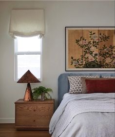 a bed sitting under a window next to a wooden dresser with a lamp on top of it