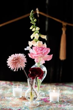 a vase with flowers and candles sitting on top of a cloth covered tablecloth next to two lit candles