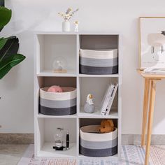 a white shelf filled with baskets next to a potted plant on top of a rug