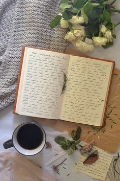 an open book sitting on top of a table next to a cup of coffee and flowers