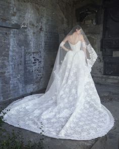 a woman in a wedding dress with a veil on her head is looking down at the ground