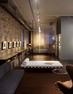 a living room filled with furniture next to a book shelf and bookshelf in front of a brick wall