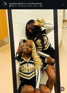 two cheerleaders are sitting on a mirror and one is taking a selfie