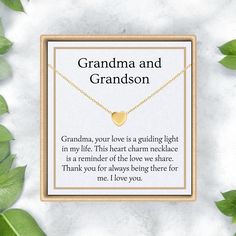 grandma and grandson necklace with gold heart on white marble background, surrounded by green leaves