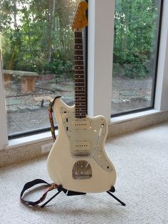 an electric guitar sitting on top of a stand in front of a window with trees outside