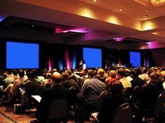 a large group of people are sitting in chairs and watching something on the screen behind them