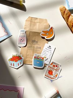 some stickers are laying on top of a table next to a bag and croissant