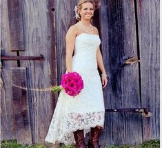 a woman standing in front of a wooden door wearing boots and holding a pink bouquet