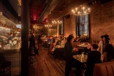 people sitting at tables in a restaurant with chandeliers hanging from the ceiling and exposed brick walls