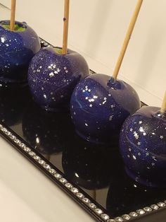 some blue apples sitting on top of a black tray with toothpicks in them