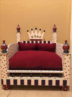 a red and white bed with a crown on it's headboard, sitting in front of a wall