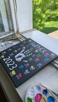 a birthday sign sitting on top of a window sill next to a plate with paint