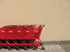 a row of red shopping carts sitting in front of a tan wall with writing on it