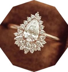 a diamond ring sitting on top of a brown velvet cushioned surface, with the center stone surrounded by smaller diamonds