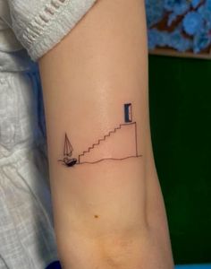 a woman's arm with a small tattoo of a sailboat on the water