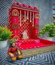 a small figurine sitting on top of a red and gold box next to potted plants