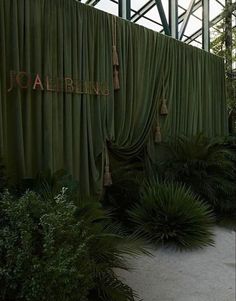 the entrance to an indoor shopping mall is covered in green curtained curtains and plants