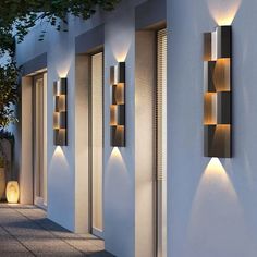 modern outdoor lighting on the side of a white building at night with trees and potted plants