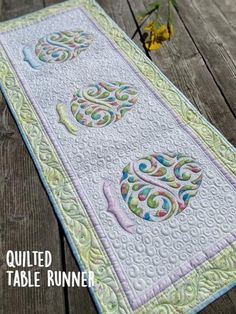 the table runner is made from quilts and has an ornate design on it, along with yellow flowers