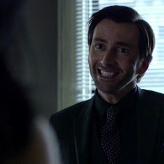 a man wearing a suit and tie in front of a window smiling at the camera