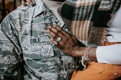 a man in camouflage jacket holding his hand on the shoulder of a woman who is wearing an orange skirt