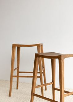 two wooden stools sitting next to each other on a white carpeted floor in front of a wall