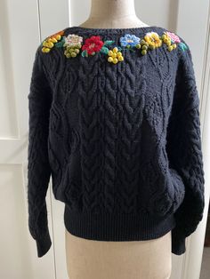 a mannequin wearing a black sweater with colorful flowers on the shoulders and sleeves