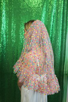 a woman wearing a veil with multicolored polka dots on it, standing in front of a green backdrop