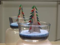 three small christmas trees are placed in glass cups