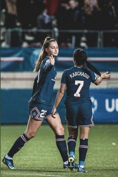 two female soccer players are standing on the field with their arms around each other as they talk