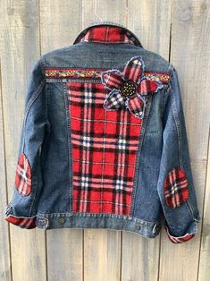 a red plaid jacket with a flower on the back, hanging up against a wooden wall