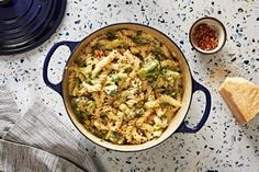 a blue pot filled with pasta and broccoli next to a slice of bread