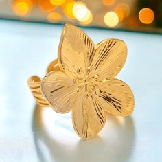 a gold flower ring sitting on top of a white table with lights in the background